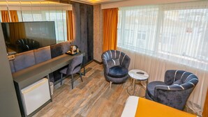 A modern hotel room with a sofa, two armchairs, a small table, a TV, and a desk with a chair. - 216 Silver Suite (Tuzla)