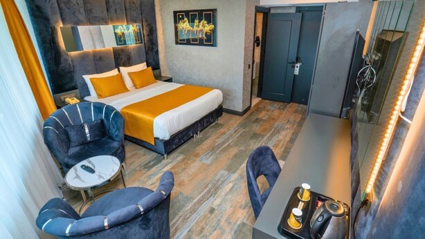 A modern hotel room with a bed, a desk, two chairs, a small table, and artwork on the walls. - 216 Silver Suite (Tuzla)