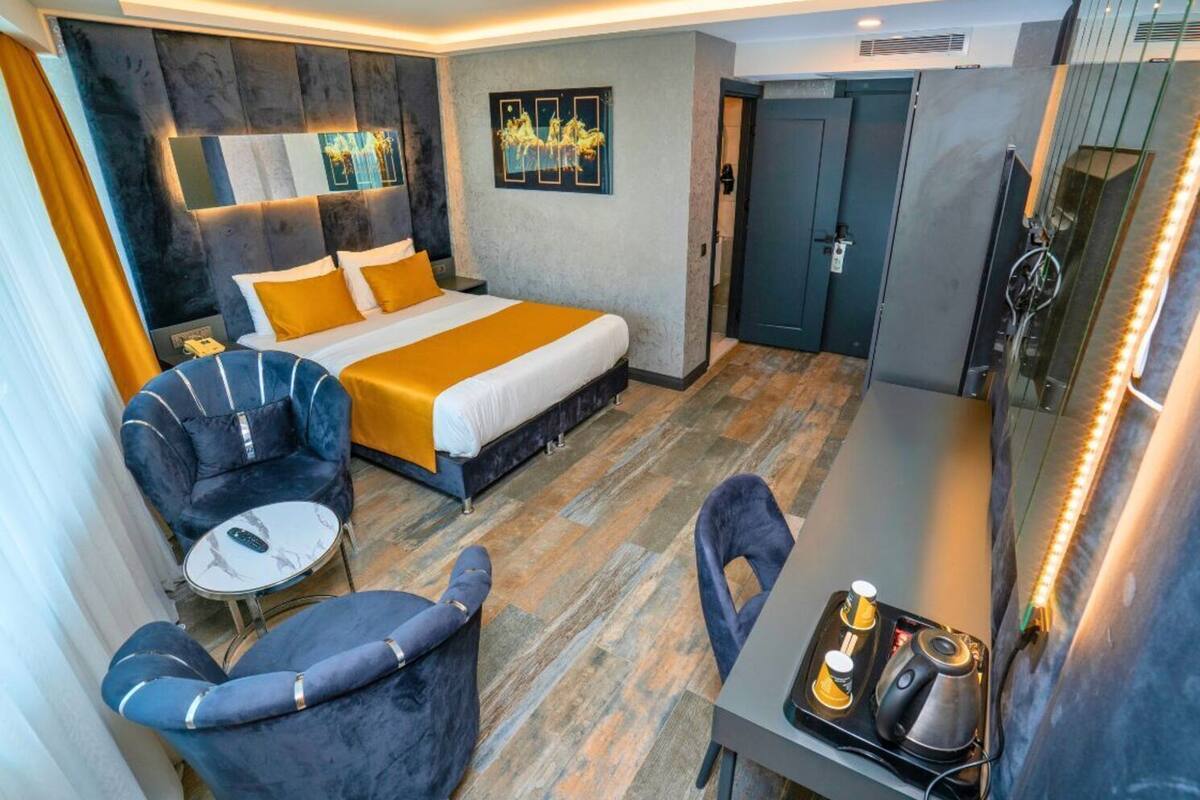Ein modernes Hotelzimmer mit Bett, Schreibtisch, zwei Stühlen, einem kleinen Tisch und Bildern an den Wänden.