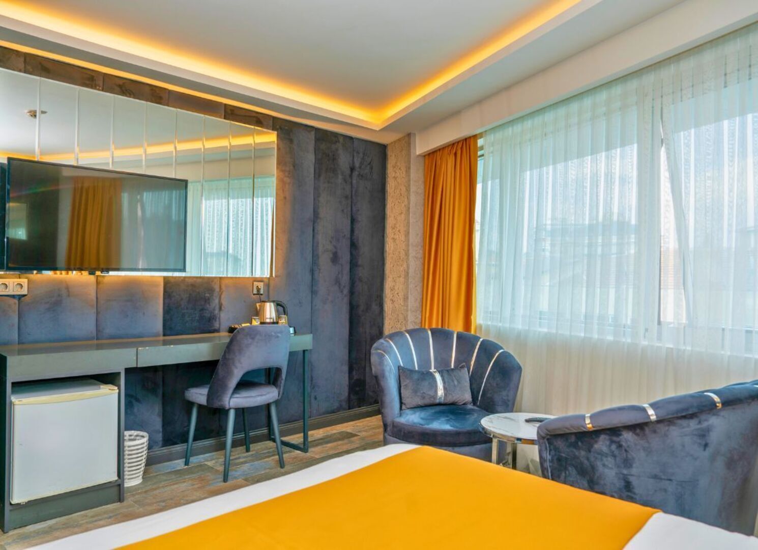 A modern hotel room with a bed, a desk, a chair, and a sofa.