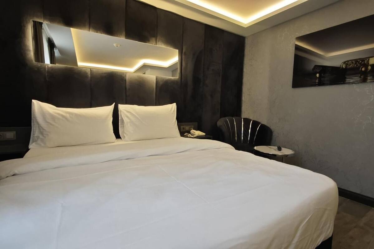 Ein modernes Hotelzimmer mit einem großen Bett, einem Nachttisch, einem Sessel und einem Wandregal.