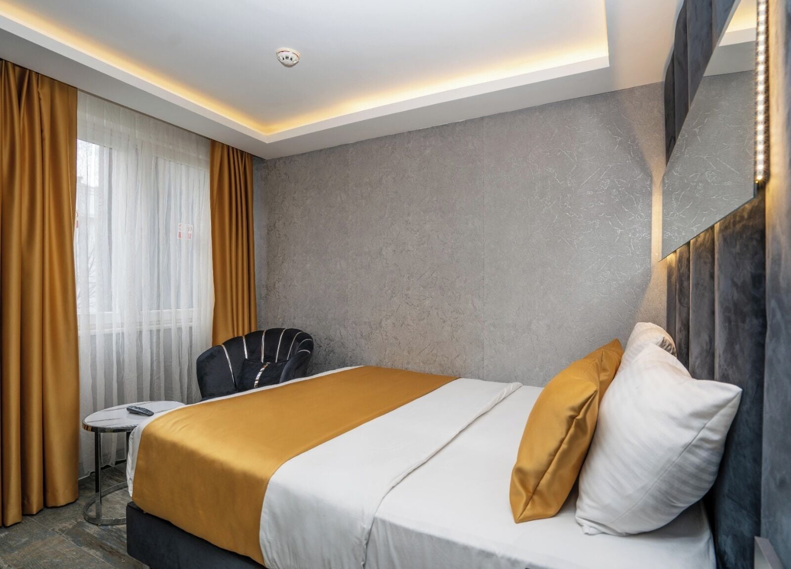 Ein modernes Hotelzimmer mit einem großen Bett, einem kleinen Tisch, einem Stuhl und Blick ins Freie.