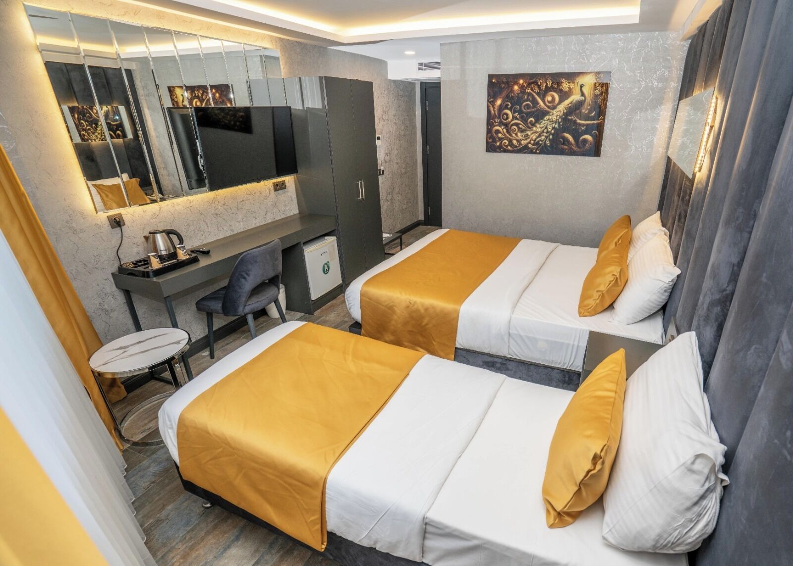 A hotel room with two beds, a desk, a chair, a small table, a mirror, and a decorative wall piece.