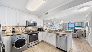 Una cocina moderna con armarios blancos, microondas integrado, horno de acero inoxidable y lavavajillas.