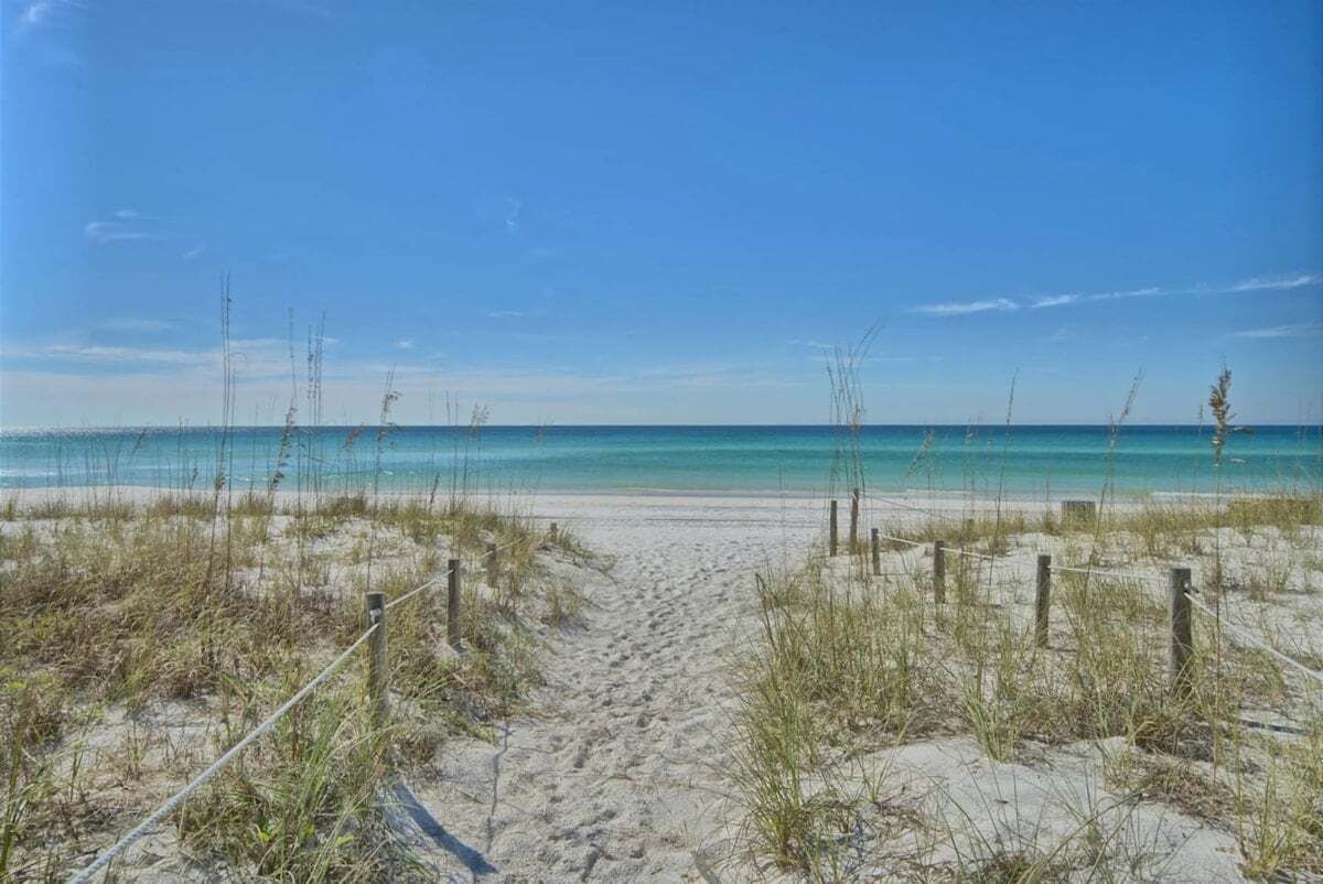 A sandy beach path leading to the ocean with a clear sky.
