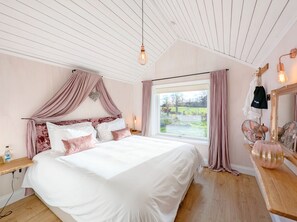 Relax in a cozy space with a large bed under a sloped ceiling, featuring a wooden nightstand and a mirror.