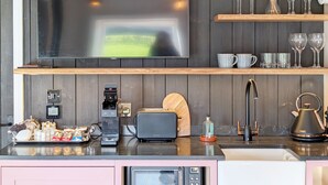 Una cocina moderna con una televisión de pantalla plana grande, estantes de madera, una cafetera, un tostador y un hervidor.
