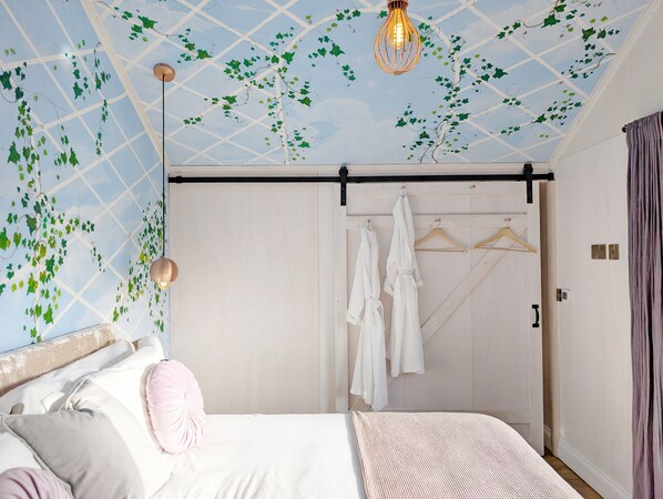 A bedroom with a bed, a hanging light fixture, and a wardrobe with hanging robes.