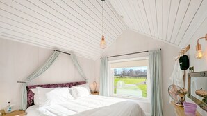 Una camera da letto con un letto, una finestra vista parco, un comodino con una lampada e una ventola a soffitto.