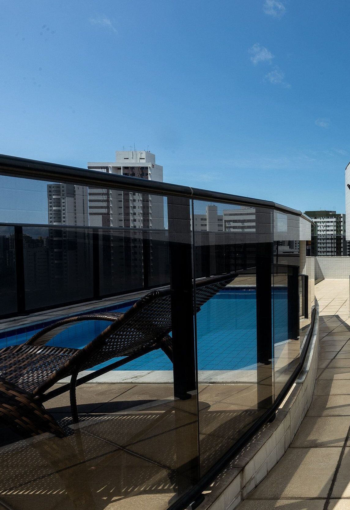Zona de piscina en la azotea con balaustrada de cristal, una tumbona y una vista despejada del horizonte de la ciudad.
