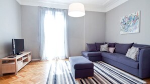 A modern living room with a sectional sofa, a flat-screen TV on a wooden stand, a striped rug, and a large window with sheer curtains. - ELEGANT APARTMENT IN THE CENTER OF BARCELONA (Barcelona)