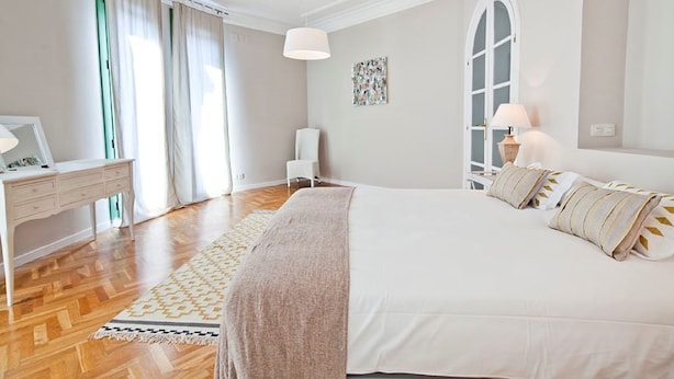 A bedroom with a large bed, a desk, and a chair. There is a window with curtains, a lamp, and a wall-mounted artwork. - ELEGANT APARTMENT IN THE CENTER OF BARCELONA (Barcelona)