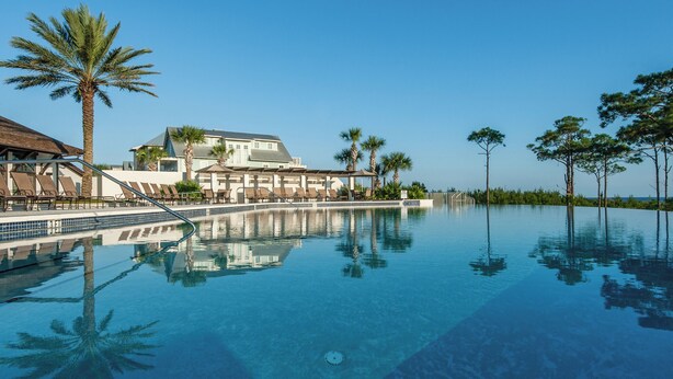 A pool with clear water, palm trees, and a building with a roof. - ☀️Infinity Pool-3BR-30A-GolfCart-4 Bikes-Screened in Porch-Beach, Please☀️ (Santa Rosa Beach)