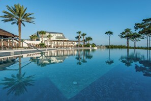 A pool with clear water, palm trees, and a building with a roof.