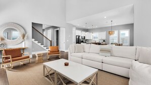 En rummelig opholdsstue med en hvid sofa, et sofabord og en lænestol. En trappe fører op til en etage ovenpå.