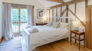 Une chambre avec un grand lit, un plafond en bois, une fenêtre avec des rideaux et une table de chevet avec une lampe.