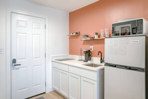 Una cocina con gabinetes blancos, un lavamanos, una cafetera y un refrigerador.