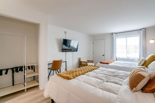 Habitación de hotel con dos camas, un escritorio, una silla, un televisor y un armario.