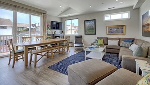 A spacious living area with a dining table, sofa, and large windows offering a view of the neighborhood. - 25%Off Sept 17-19 Walk 2 Beach, Amazing Ocean View (Ventura)