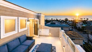 A balcony with a sofa, a glass door, and a view of the sunset over the ocean. - 25%Off Sept 17-19 Walk 2 Beach, Amazing Ocean View (Ventura)