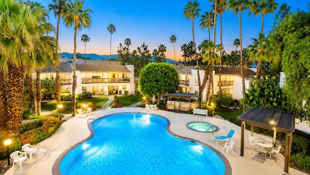 A swimming pool with lounge chairs, surrounded by palm trees and a building with multiple balconies.