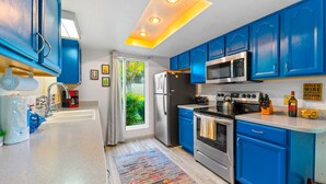 A modern kitchen with blue cabinets, stainless steel appliances, and a large window.
