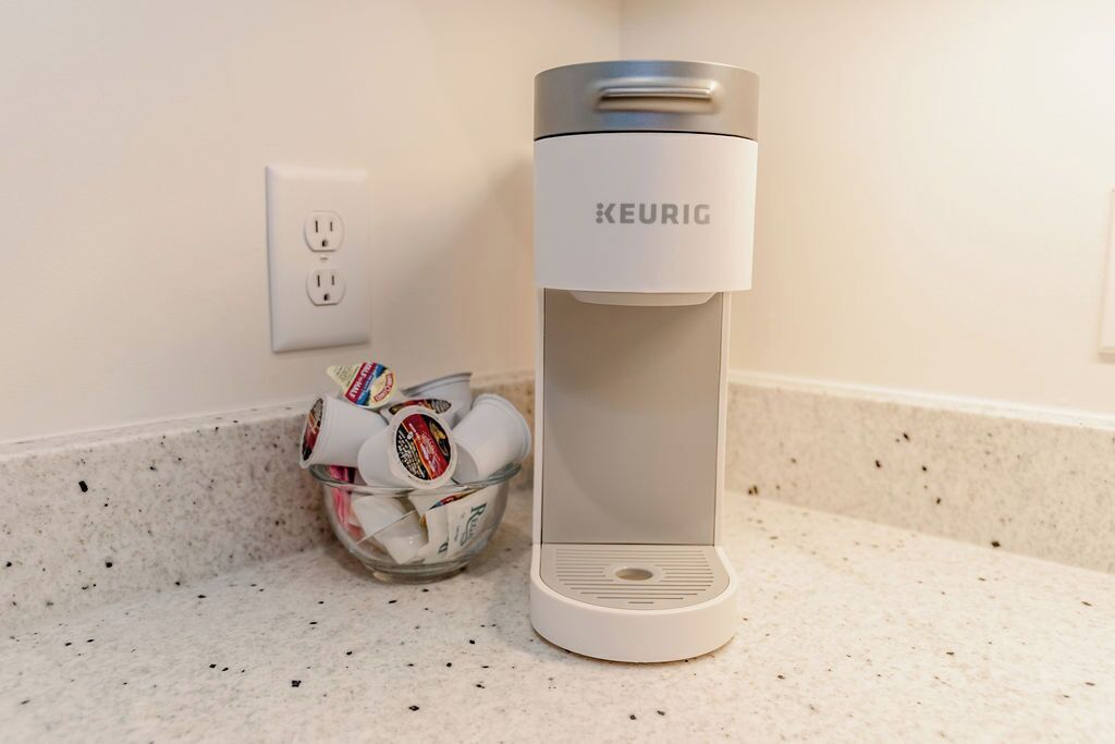 A Keurig coffee maker on a countertop next to a glass container holding coffee pods.