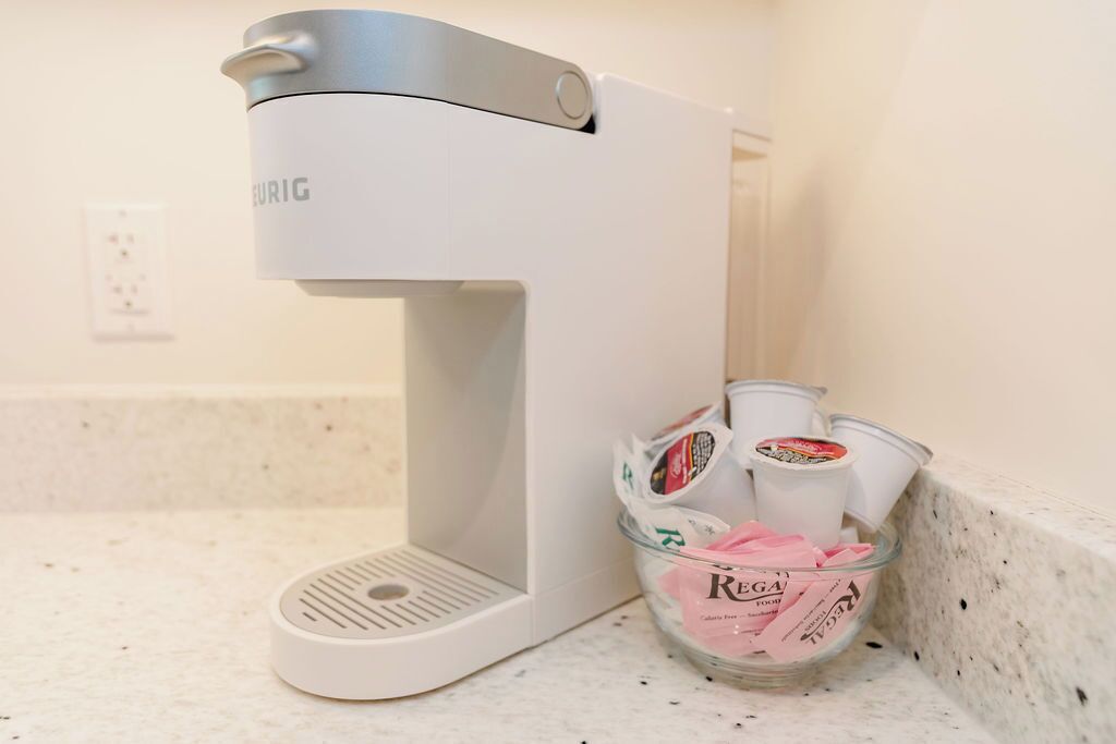 A white coffee maker with a cup holder on a kitchen counter.