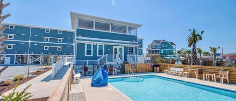 A pool area with a wooden deck, lounge chairs, and a building with multiple windows and balconies.
