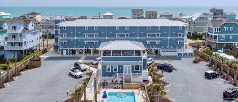 A beachfront hotel with a swimming pool, multiple balconies, and a view of the ocean.