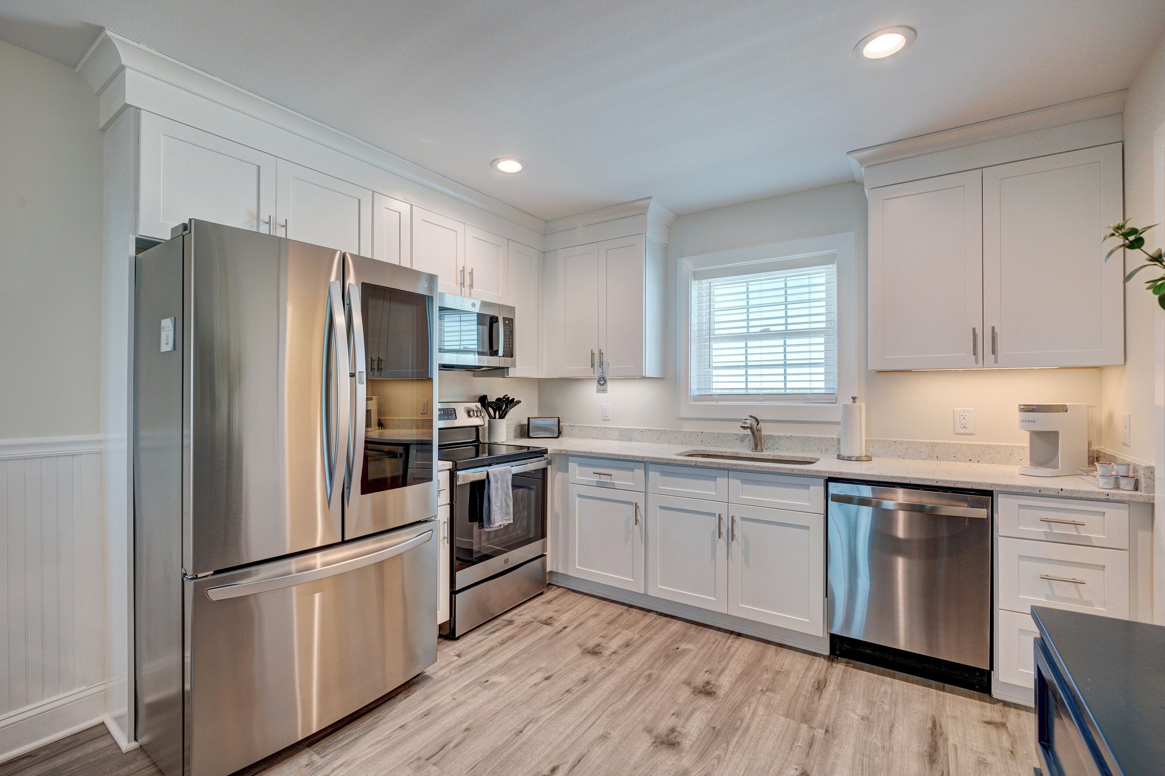 A modern kitchen with white cabinetry, stainless steel appliances, and a wooden floor.