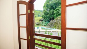 A wooden door leading to a balcony with a view of a pool and lush greenery. - Sana Spa Maria Bonita (Macaé)