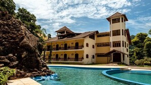 A large building with multiple balconies and a tower, surrounded by a swimming pool and greenery. - Sana Spa Maria Bonita (Macaé)