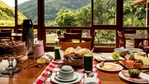 A breakfast setting with a table set for two, featuring a variety of food items and a coffee pot. - Sana Spa Maria Bonita (Macaé)