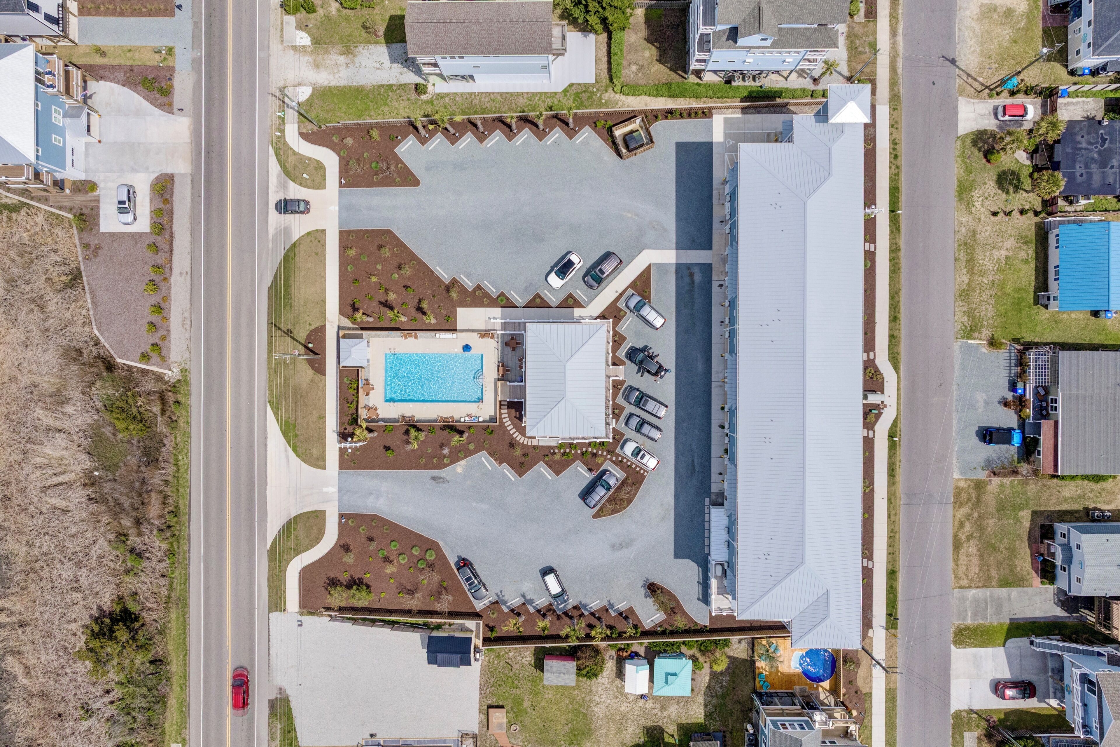 An aerial view of a residential area with a large swimming pool, multiple driveways, and a road.