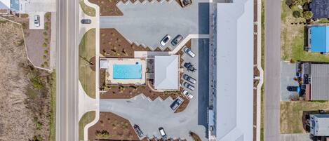 An aerial view of a residential area with a large swimming pool, multiple driveways, and a road.