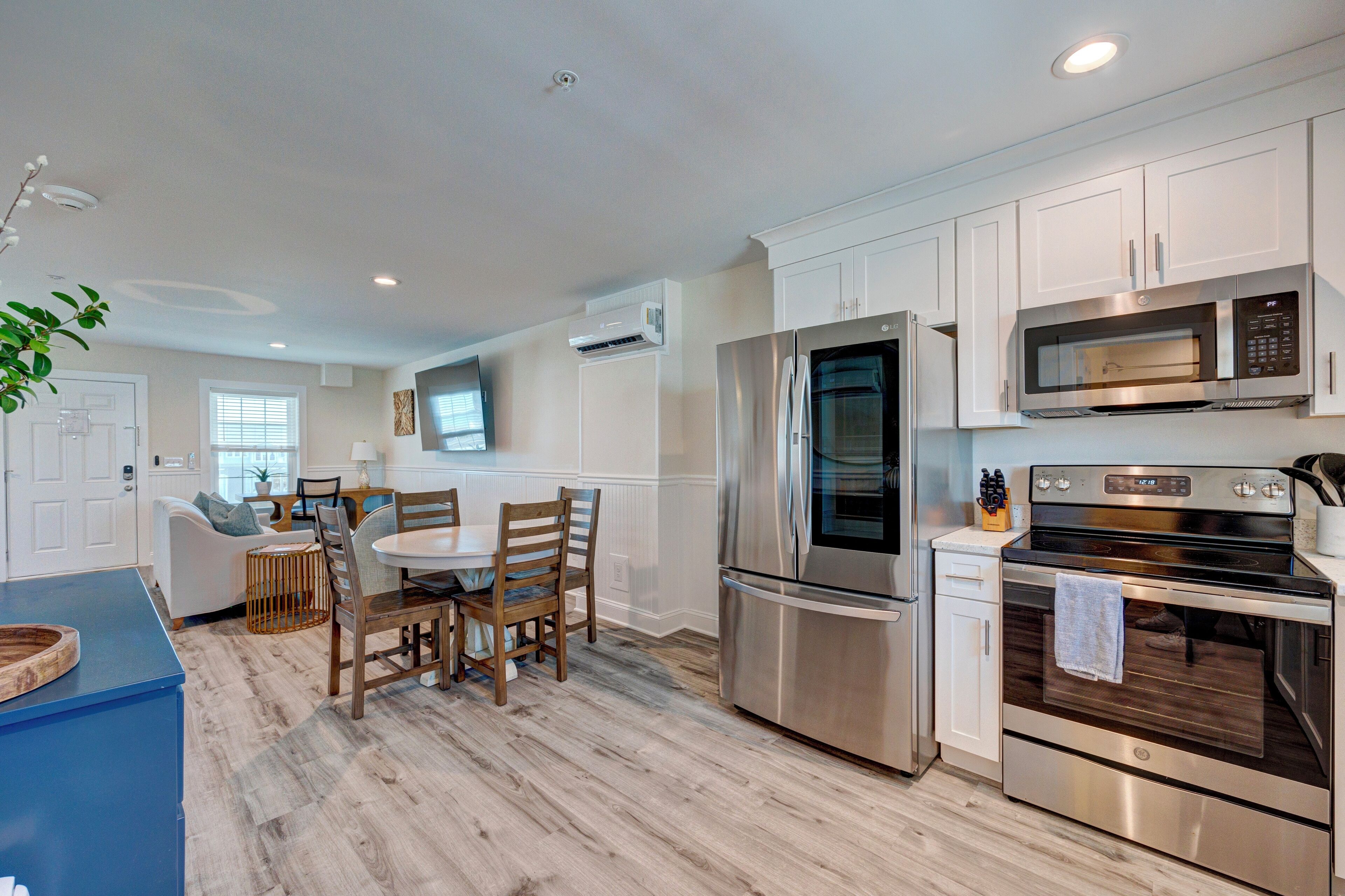 A modern kitchen with stainless steel appliances, a dining area with wooden chairs, and a blue accent wall.