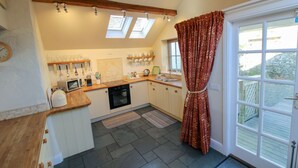 A kitchen with a wooden countertop, a microwave, a sink, and a window with curtains.