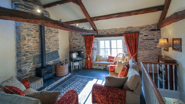 A cozy living room with a stone fireplace, wooden beams, a comfortable sofa set, and a television.