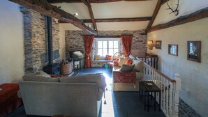A cozy living room with a stone wall, a fireplace, a sofa, a television, and a staircase with a railing.
