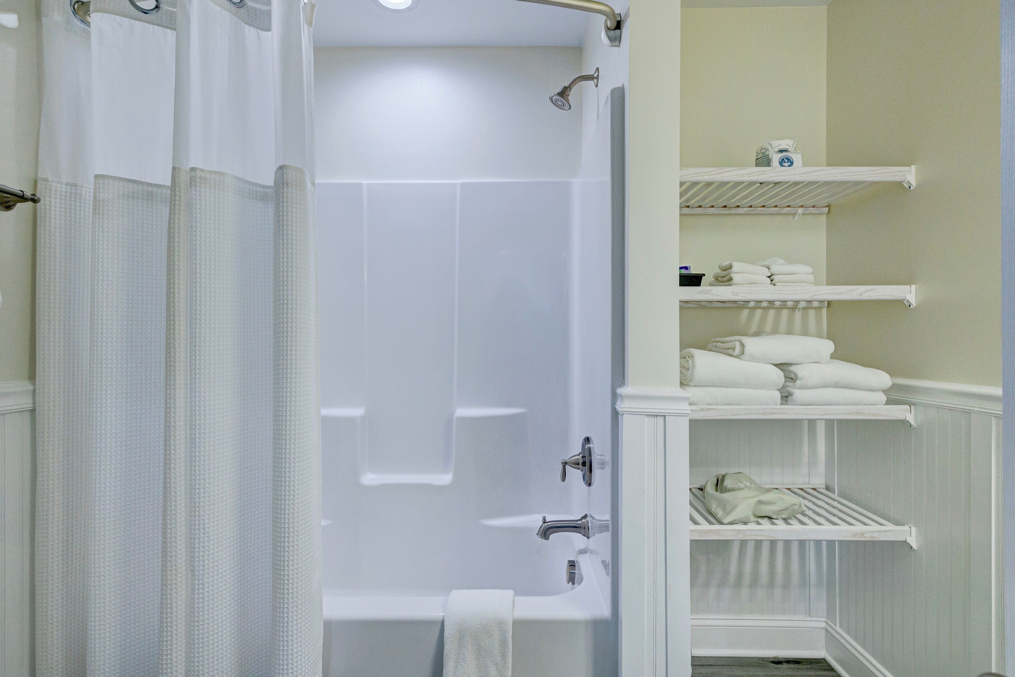 Une salle de bain avec une baignoire, un rideau de douche et des étagères où sont rangées les serviettes.