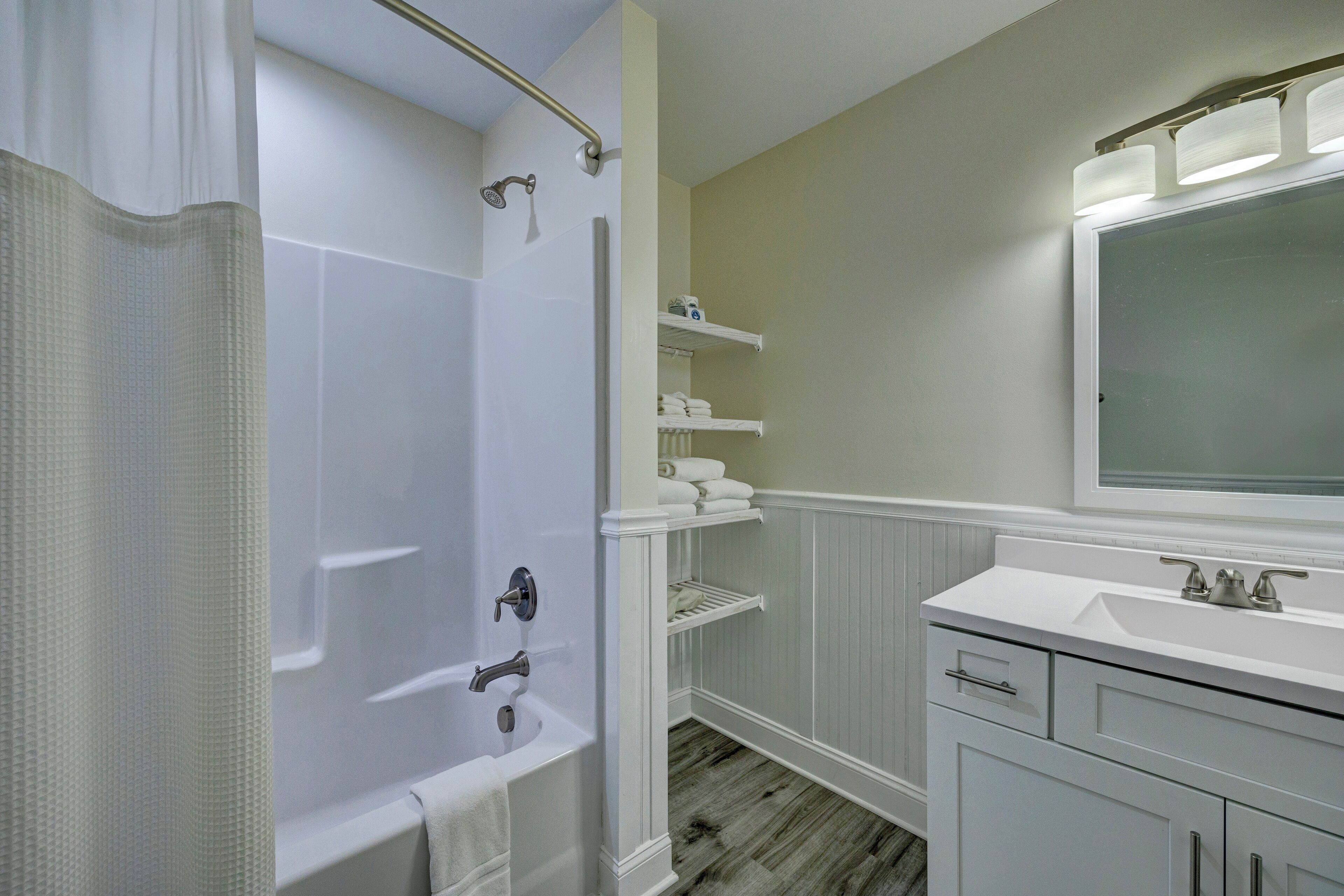 A bathroom with a bathtub, a shower, a vanity with a mirror, and built-in shelves.
