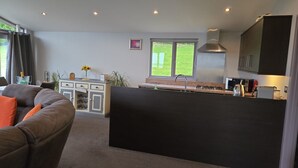 A modern kitchen with a large island, a dining area with a sofa, and a view of the outdoors through a window. - Haven Lodge Kirkby In Furness -  a lodge that sleeps 2 guests  in 1 bedroom (Kirkby in Furness)