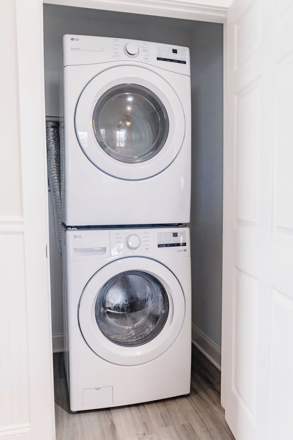 Une machine à laver et un sèche-linge superposés dans une pièce aux murs blancs et au plancher en bois.