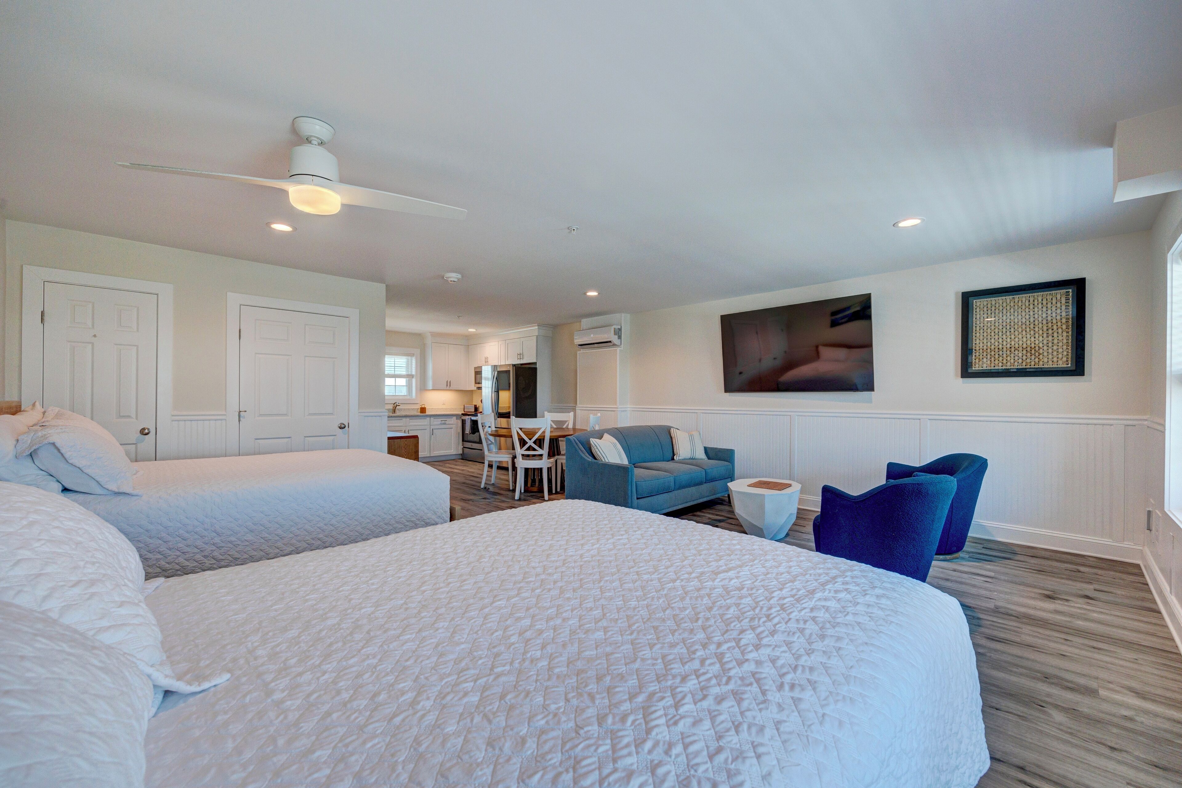 A hotel room with two beds, a dining area, and a living area with a blue sofa and chairs.