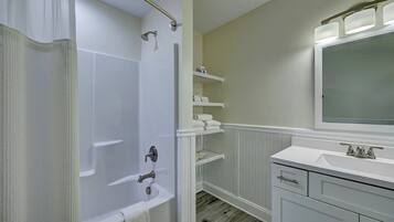 Een badkamer met een bad, douche, wastafel met spiegel en inbouwkasten.