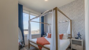 Ein Himmelbett mit Baldachin, ein Nachttisch mit einer Dekoration und Blick durch das Fenster.