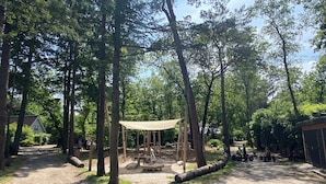 A forested campsite with a canopy shelter, picnic tables, and a dirt path. - Luxury Holiday Home Vosje on the Veluwe in a Small-Scale Forest Park in Nunspeet (Nunspeet)