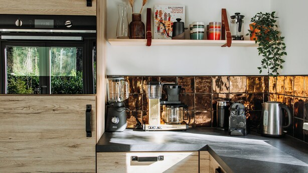 A modern kitchen with wooden cabinetry, a built-in oven, and various appliances like a blender and coffee maker. - Luxury Holiday Home Vosje on the Veluwe in a Small-Scale Forest Park in Nunspeet (Nunspeet)