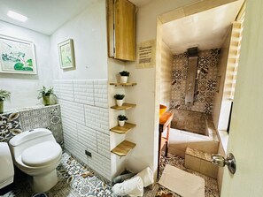 A bathroom with a white toilet, patterned tiles, a wooden shelf with plants, and a tiled shower area. - Ecohotel Zona 7 (Rionegro)